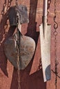 On the rusty metal wall of the village shed hang on the chains used old vintage agricultural shovels Royalty Free Stock Photo