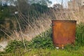 a metal garbage bin on a riverbank with soft focus background