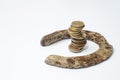 Rusty old horse shoe with a tall stack of coins on white background Royalty Free Stock Photo