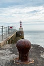 Rusty old mooring point on a jetty with red and white striped lighthouse in the background Royalty Free Stock Photo