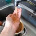 Rusty orange water flows from the kitchen faucet onto a man& x27;s hand Royalty Free Stock Photo