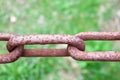 Rusty oxidized brown link of an old strong forged metal iron chain against a background of green