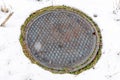 Rusty round storm drain manhole cover on snow covered grassy land in winter Royalty Free Stock Photo