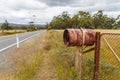 Rusty rural barrel letterbox on farm gate near country road