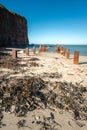 Rusty steel beams, remnants of old ocean pier, on the beach of Helgoland island, Germany. Tall red cliffs in the