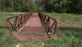 Rusty pedestrian bridge with grate floor as pathway across artificial water channel and triangular shaped railing Royalty Free Stock Photo