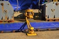 A rusty yellow mooring bitt, mooring line and dark blue bulwark of a dredger