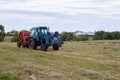 Rybushkino village, Russia - July 1, 2020: Close-up blue tractor collects hay from dry clover grass. Haymaking and harvesting