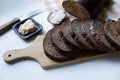 Rye bread is cut into slices on a wooden board on a light background, near butter, a knife, a loaf of bread, butter is spread on o Royalty Free Stock Photo