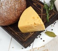 Rye bread and a triangle of cheese lie on a dark board on a wooden white table, top view