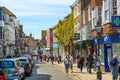 High street of Old Rye town with periodic buildings, lots of people and cars parked on side.