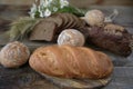 Rye and wheat fresh hot bread with ears and a bouquet of daisies on a wooden rustic background, close-up. Royalty Free Stock Photo