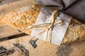 Rye whole wheat bread roll with golden crust wrapped in parchment paper on wood vintage box, grey linen napkin