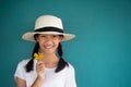 11s Asia girl or young women in white t-shirt and summer hat holding yellow wild spring flower on green blue cement wall Royalty Free Stock Photo