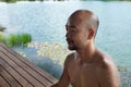 40s bald beard man eye closing mediation with summer blue water lake in wellness relaxation background