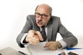 60s bald senior office boss man furious and angry gesturing upset and mad sitting on desk with paperwork in business and job prob Royalty Free Stock Photo