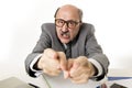 60s bald senior office boss man furious and angry gesturing upset and mad sitting on desk with paperwork in business and job prob Royalty Free Stock Photo