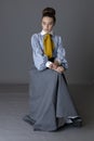 An Edwardian working class woman wearing a striped cotton blouse, mustard yellow cravat, and a grey walking skirt