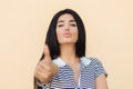 That`s fine! Lovely healthy female with dark hair, looks confidently at camera, raises thumb as shows like gesture, approves somet