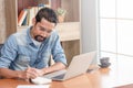 30s handsome businessman take a short note on paper while reading article from internet.  Modern arab businessman in casual Royalty Free Stock Photo