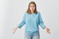 It`s not a big deal. Clueless cute girl dressed in blue sweater and jeans shrugging shoulders and staring at camera with