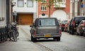 dark grey classic Cadillac DeVille hearse parked on narrow city street.