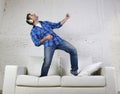 20s or 30s man jumped on couch listening to music on mobile phone with headphones playing air guitar Royalty Free Stock Photo