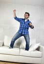 20s or 30s man jumped on couch listening to music on mobile phone with headphones playing air guitar Royalty Free Stock Photo