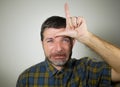 30s or 40s unshaven sad and ashamed man doing loser sign with hand and fingers on his front in funny depressed face expression in Royalty Free Stock Photo