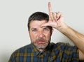 30s or 40s unshaven sad and ashamed man doing loser sign with hand and fingers on his front in funny depressed face expression in Royalty Free Stock Photo