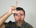 30s or 40s unshaven sad and ashamed man doing loser sign with hand and fingers on his front in funny depressed face expression in Royalty Free Stock Photo