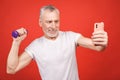 It`s selfie time! Close-up portrait Of A Senior Man Exercising with dumbbells against red Background. Using phone Royalty Free Stock Photo