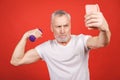 It`s selfie time! Close-up portrait Of A Senior Man Exercising with dumbbells against red Background. Using phone Royalty Free Stock Photo