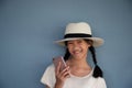 10s smiling long hair Asian girl holding pink mobile phone and wearing hat with blue concrete background