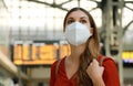 It`s time to go back to travel. Close up of traveler girl wearing KN95 FFP2 face mask at train station. Young caucasian woman wit