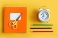 It`s time to go to school: a stack of multi-colored notebooks, multi-colored pencils, scissors, a white alarm clock on a yellow Royalty Free Stock Photo