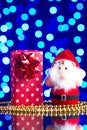 Santa Claus toy, gift in package and golden beads on a glass table with a beautiful blue bokeh Royalty Free Stock Photo