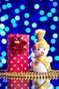 Snowman toy, gift in package and golden beads on a glass table with a beautiful blue bokeh Royalty Free Stock Photo