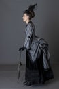 A Victorian woman wearing a striped silk polonaise and a black skirt and standing against a studio backdrop Royalty Free Stock Photo