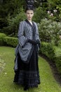 A Victorian woman wearing a striped silk polonaise and a black skirt and standing in a summer garden Royalty Free Stock Photo