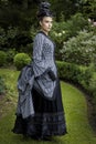 A Victorian woman wearing a striped silk polonaise and a black skirt and standing in a summer garden Royalty Free Stock Photo