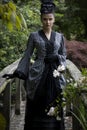 A Victorian woman wearing a striped silk polonaise and a black skirt and standing in a summer garden Royalty Free Stock Photo