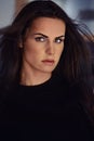 25s woman portrait with fluttering black hairs looking at camera posing indoors