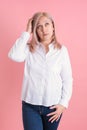 A 40s woman thoughtfully scratches her head while standing on a pink background Royalty Free Stock Photo
