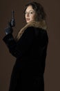 A 1920s woman wearing a black velvet coat, holding a gun, and standing against a brown backdrop Royalty Free Stock Photo