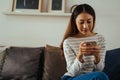 30s young adult Asian woman playing a mobile phone sits on sofa in the living room at home. Happy female internet and