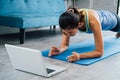 20s young Asian woman in sportswear doing plank poses while watching fitness training class on computer laptop online Royalty Free Stock Photo