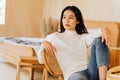 20s young teenage Asian woman wears a sweater looking away in stylish cozy room background. Attractive female model