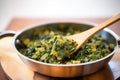 saag aloo being stirred in a pan with a wooden spoon