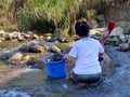 Sabah, Malaysia - March 18, 2024 : A young housewife doing laundry in a river during dry season in Ranau, Sabah, Malaysia.